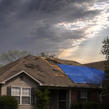 Shingled roof with storm damage under a clearing sky